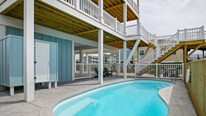 Piscina com deck de madeira e guarda-corpos brancos, cercada por área coberta com vista para outros edifícios.