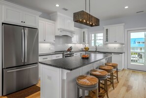Een moderne keuken met witte kasten, een roestvrijstalen koelkast, een centraal eiland met krukken en een hangende lamp.