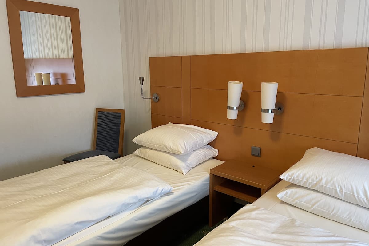 Une chambre d’hôtel avec deux lits simples, une tête de lit en bois, des lampes de chevet et un miroir au mur.