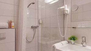 Ein modernes Badezimmer mit Duschkabine aus Glas, einer Handbrause, einem an der Wand montierten Föhn und einem kleinen Topfpflanzen auf dem Waschtisch.