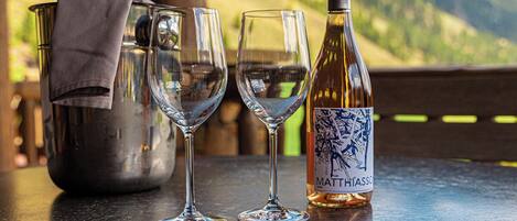 A bottle of Matt Hiasch wine, two glasses, and a metal bucket on a table with a mountain view in the background.