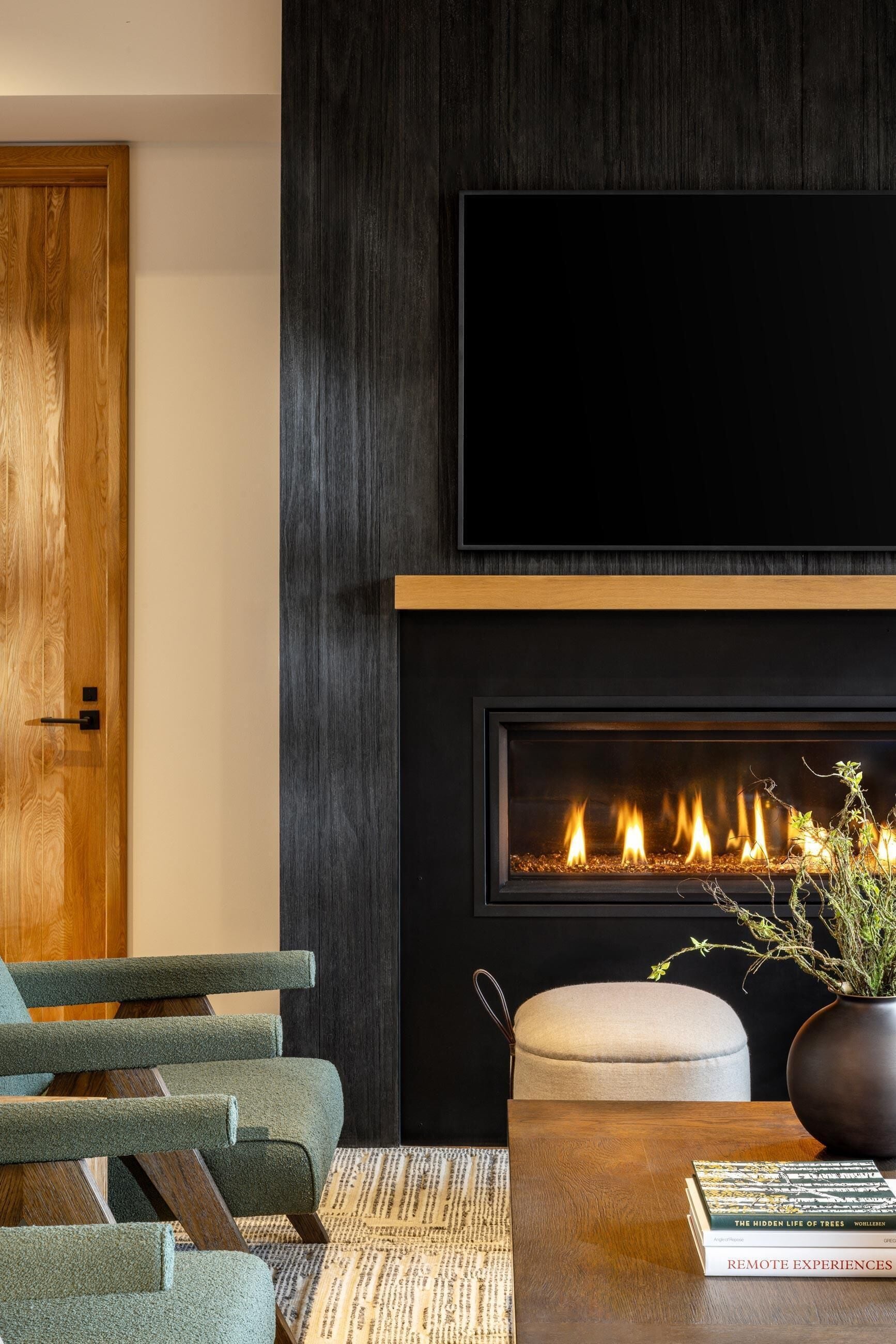 Ein modernes Wohnzimmer mit Kamin, einem darüber hängenden Fernseher und einer Sitzecke mit Sofa und Hocker.