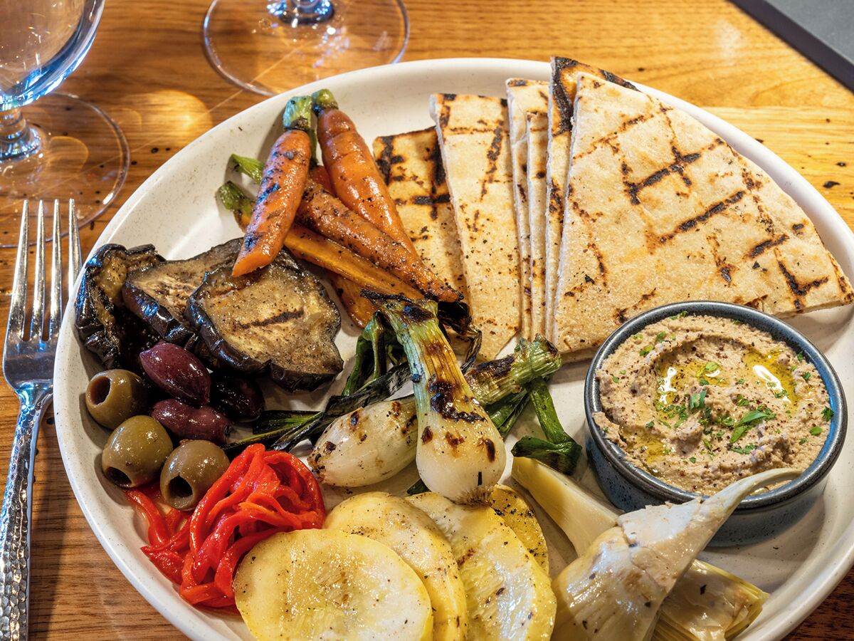 En tallrik med grillade grönsaker, tunnbröd och en skål med hummus.