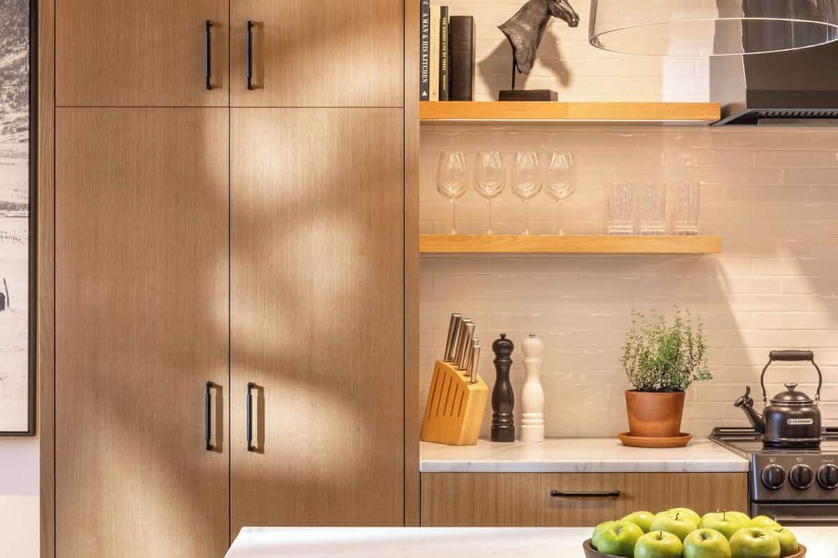 A modern kitchen with wooden cabinets, a marble countertop, and a central island with a bowl of apples.