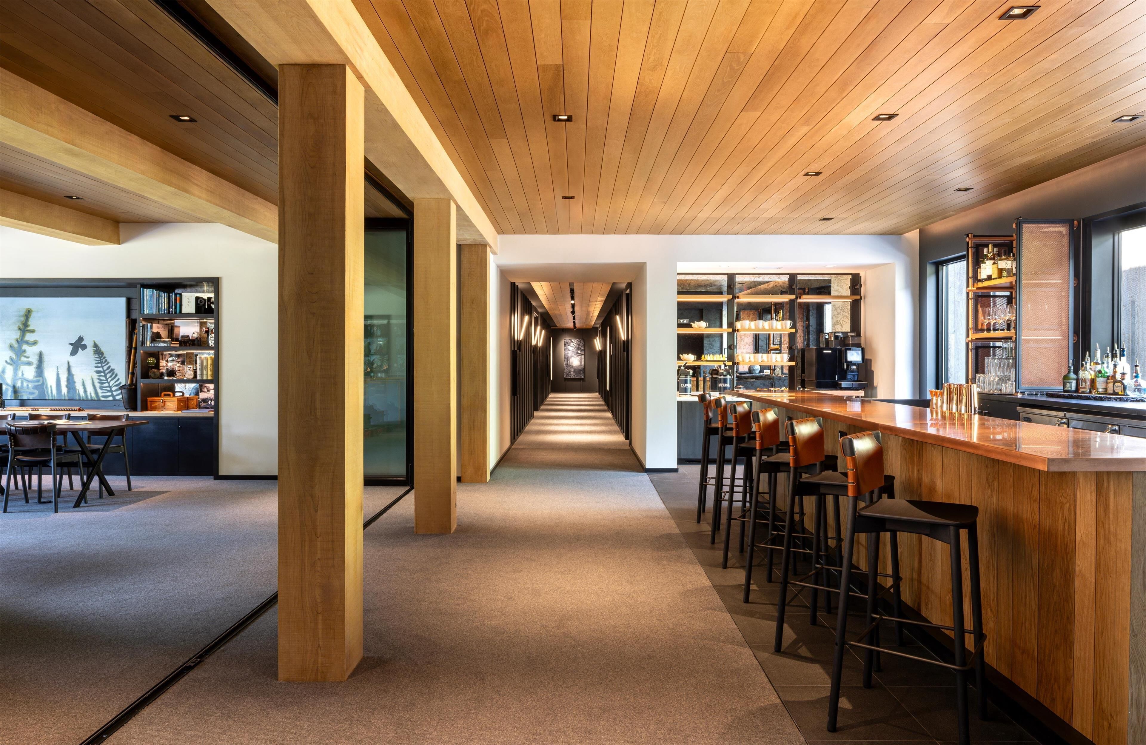 A modern bar area with a long counter, multiple stools, and a view of the bar area through a glass partition.