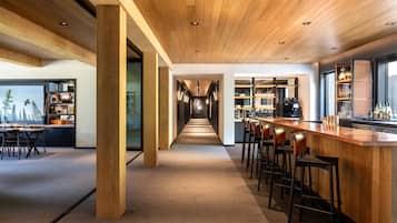 A modern bar area with a long counter, multiple stools, and a view of the bar area through a glass partition.