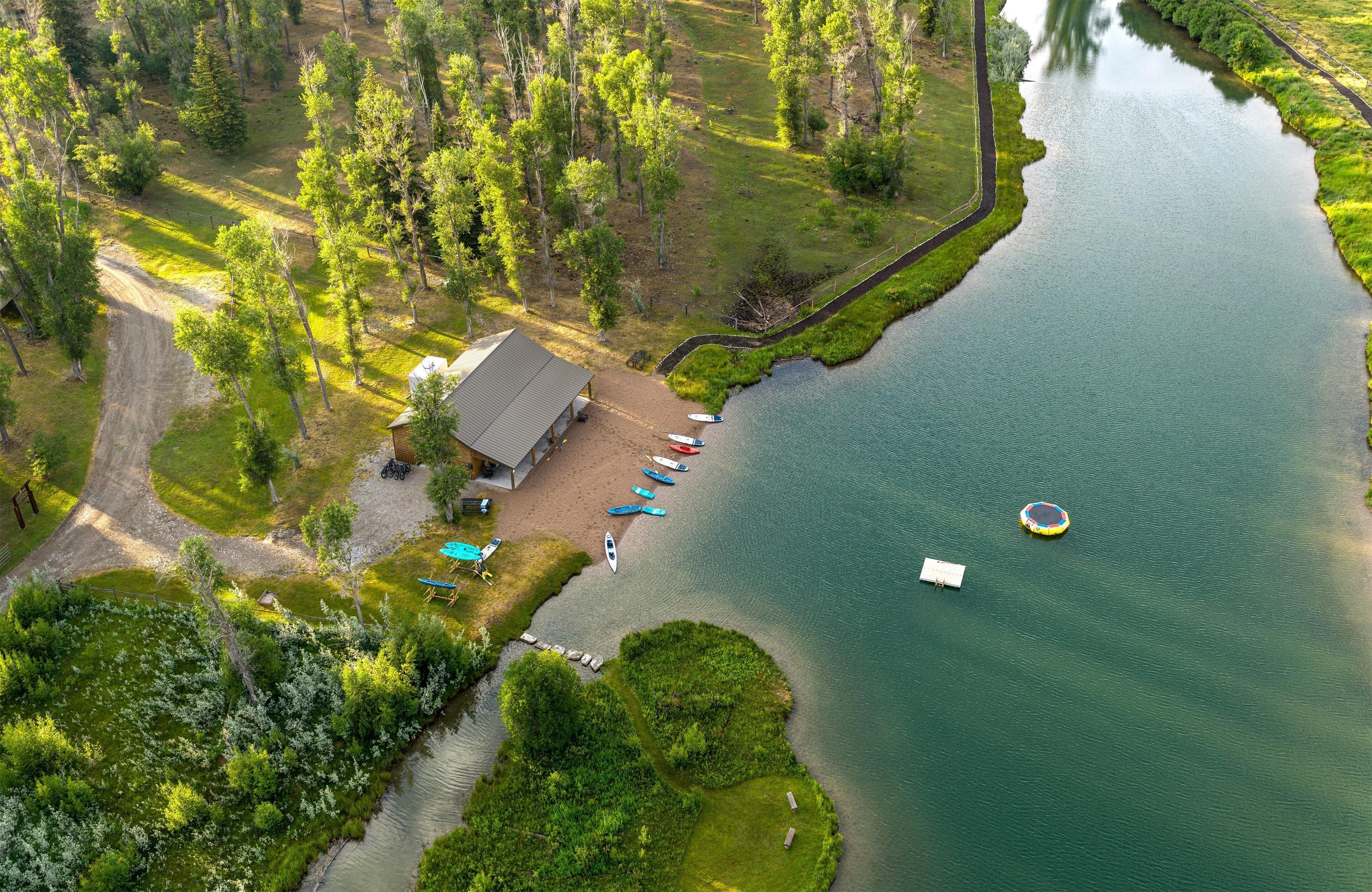 An aerial view of a lakeside property with a dock, boats, and a building with a sloped roof.