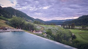 Piscina con una chimenea y sillones de descanso, rodeada de un paisaje montañoso y un campo de golf.