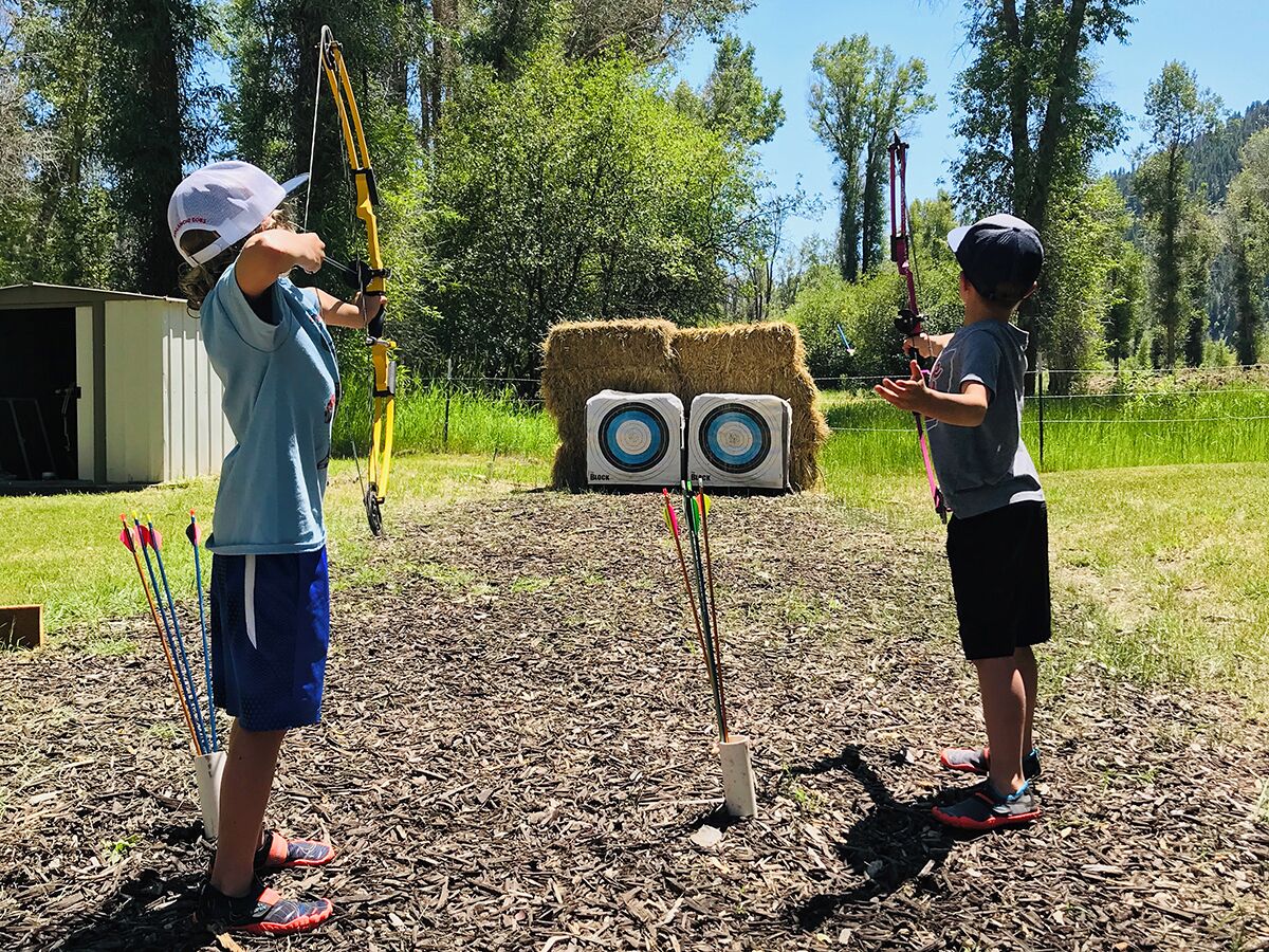 Dos personas practicando tiro con arco en un área al aire libre con césped.