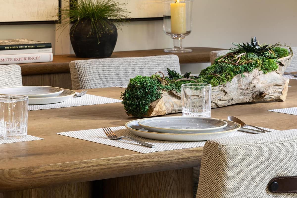 A dining area with a wooden table set for two, a candle centerpiece, and a framed painting of a snowy landscape.