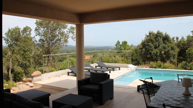 Zona piscina con lettini, un tavolo e vista sul paesaggio circostante.
