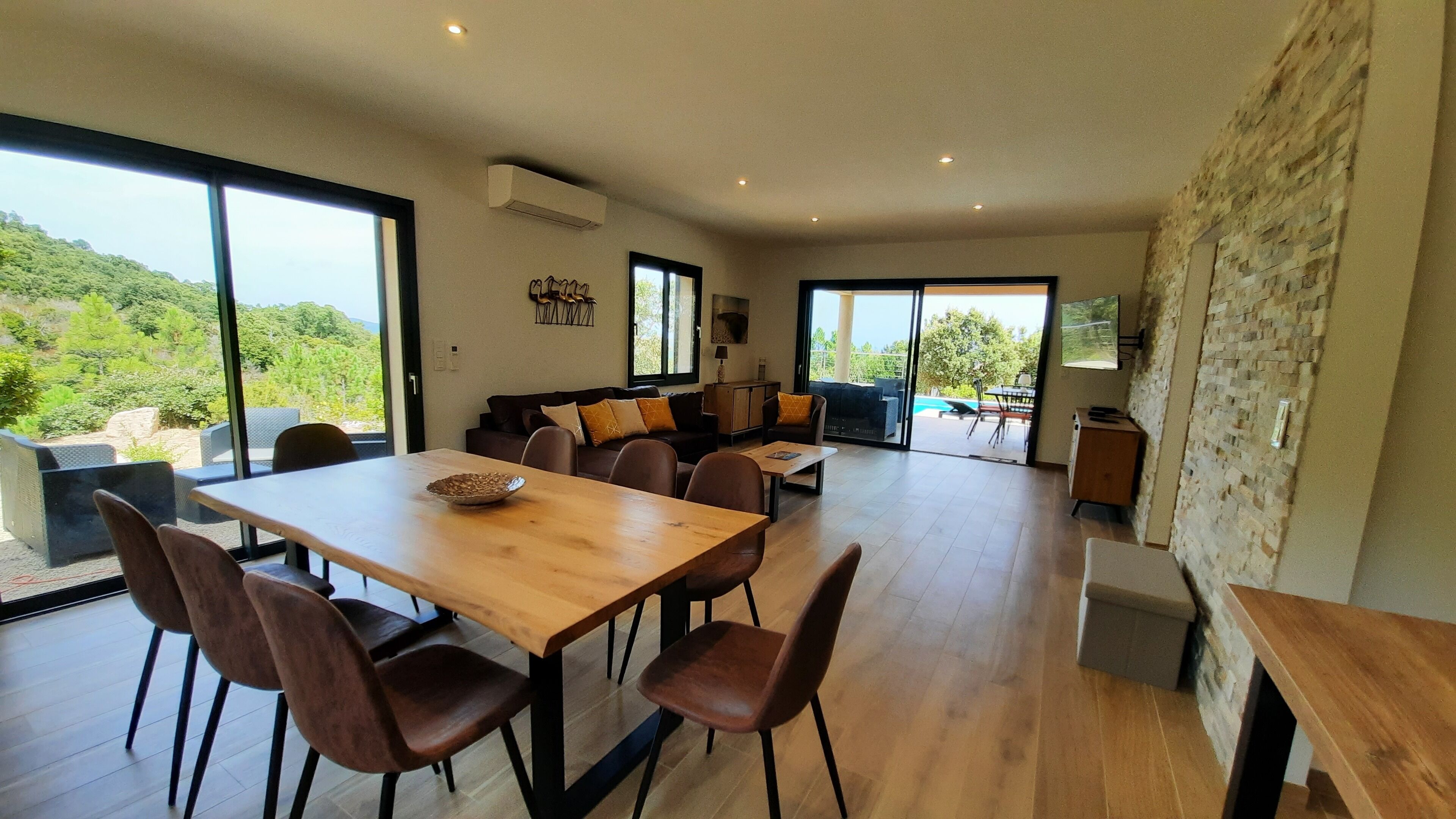 Un salón espacioso con una mesa de comedor de madera, asientos cómodos y grandes ventanales que ofrecen vistas al exterior.