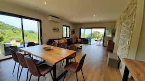 Un'ampia zona giorno con tavolo da pranzo in legno, posti a sedere confortevoli e ampie finestre con vista sull'esterno.