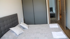 Una camera da letto con un letto, cuscini, un armadio e un bagno visibile attraverso una porta aperta.