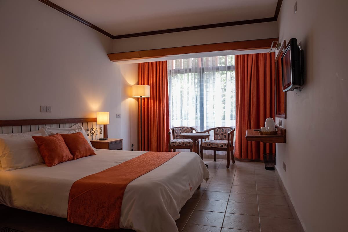 Une chambre d’hôtel avec un grand lit, un bureau avec une chaise, un téléviseur fixé au mur et une fenêtre avec des rideaux.