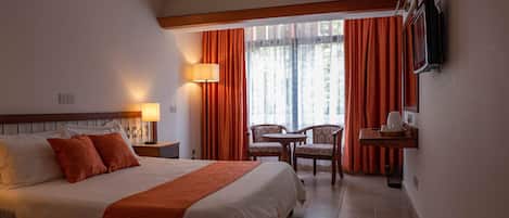 A hotel room with a large bed, a desk with a chair, a TV mounted on the wall, and a window with curtains.