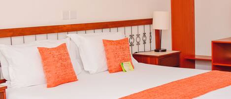 A hotel room with a large bed, white bedding, and orange accents.