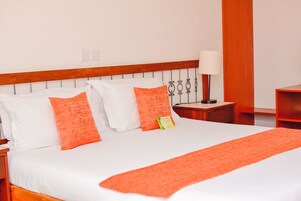 Una habitación de hotel con una cama grande, ropa de cama blanca y detalles en naranja.