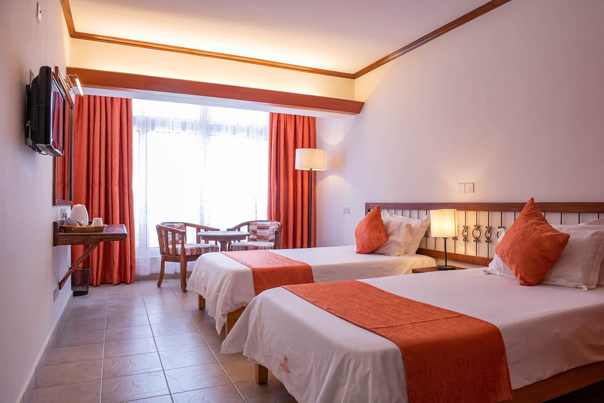 Une chambre d’hôtel avec deux lits, une télévision, un bureau avec une chaise et une fenêtre avec des rideaux.