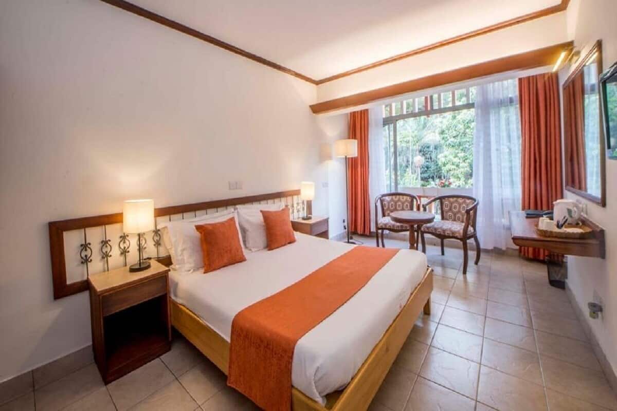 Une chambre d’hôtel avec un grand lit, des tables de chevet, une chaise, une petite table et une fenêtre avec des rideaux.