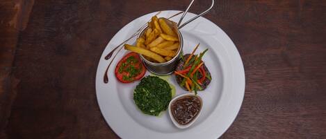 A plate with French fries, a tomato, a green salad, and a small bowl of sauce.