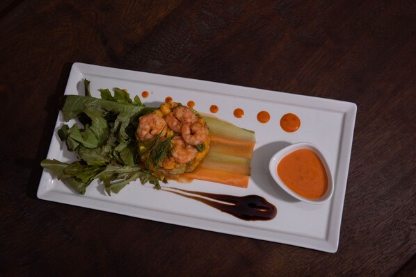 Plato rectangular blanco con un plato de camarones, vegetales y dos salsas sobre una mesa de madera oscura.