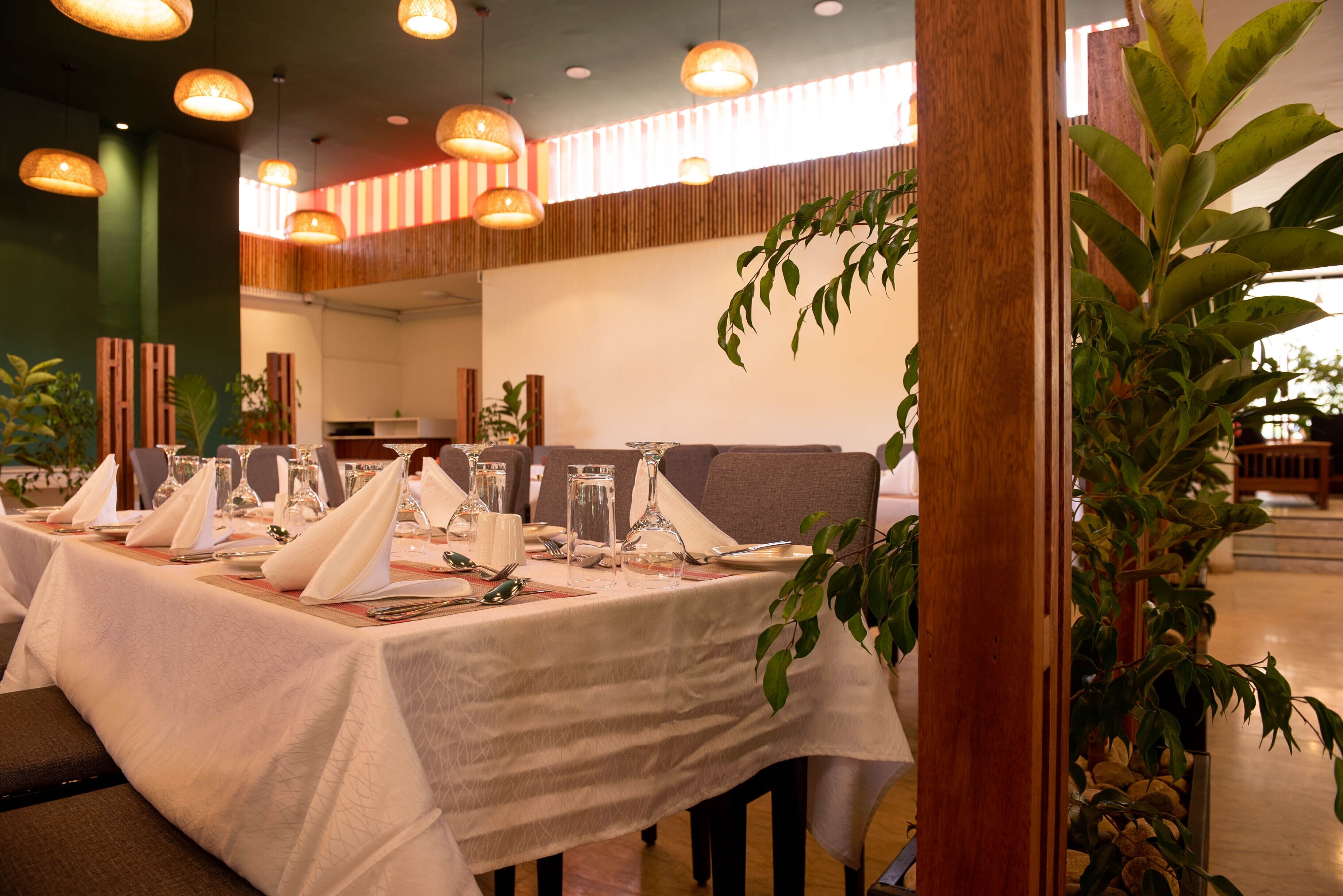 A dining area with tables set for a meal, featuring a modern interior with wooden accents and hanging pendant lights.