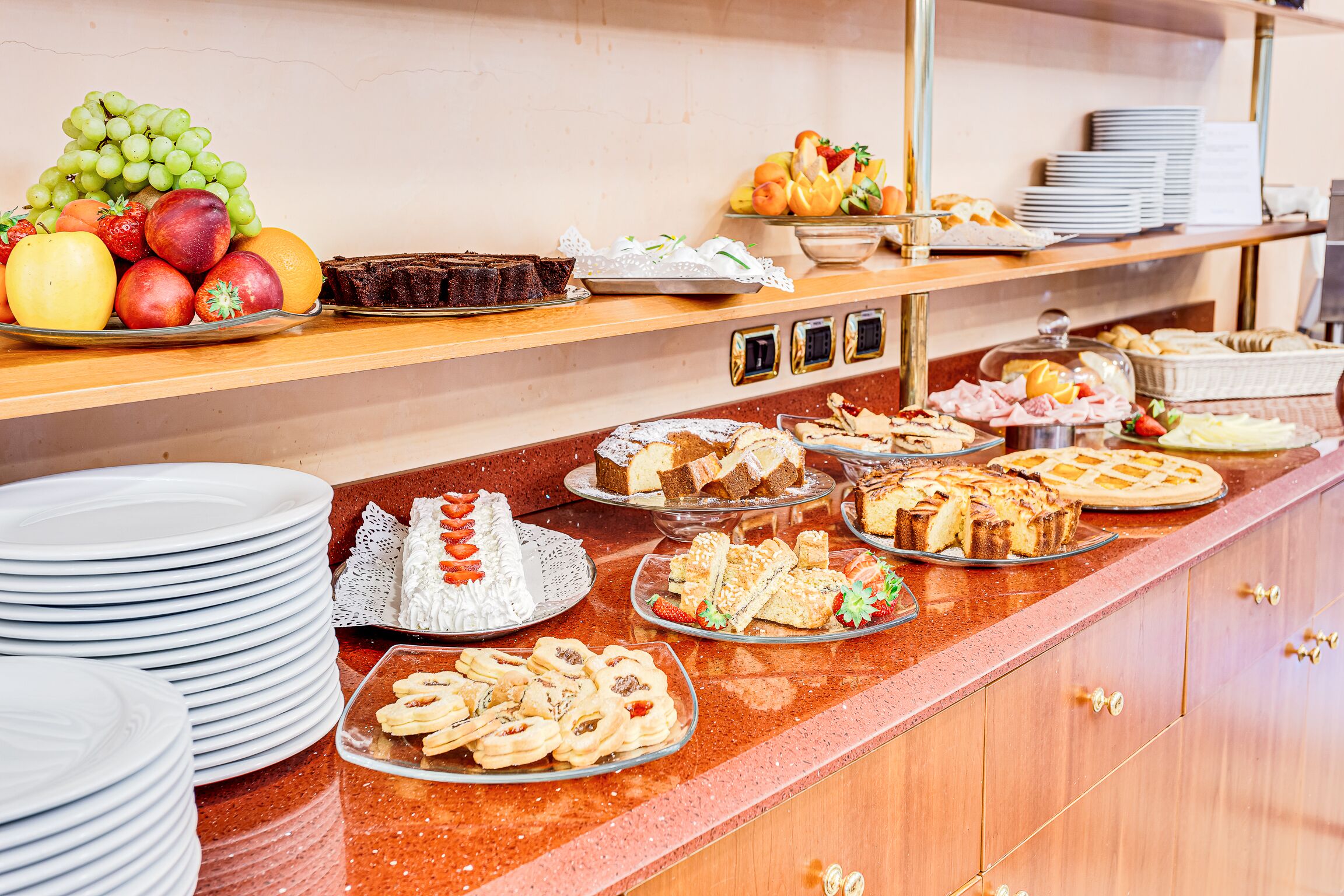 Un bufé con diversas opciones de comida, entre ellas frutas, pasteles y postres.