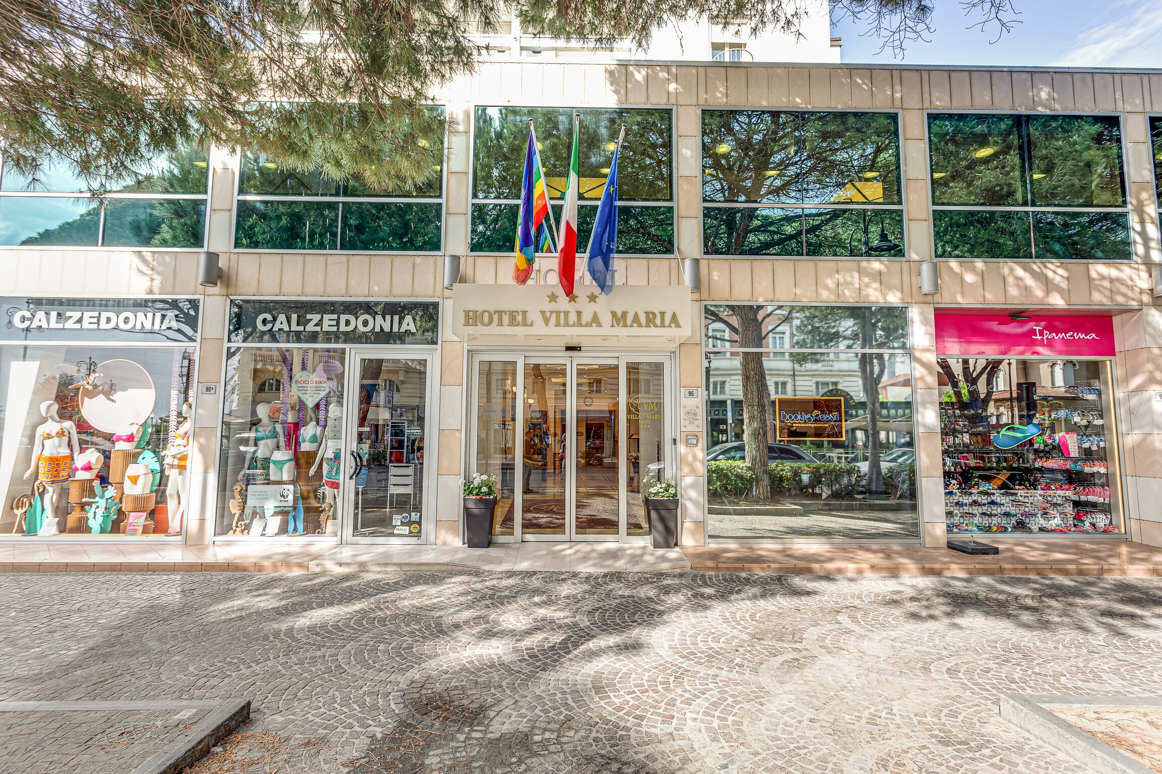 A hotel entrance with flags, a storefront named Calzedonia, and a shop called Ipanema.
