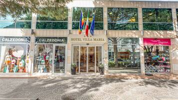 Entrada de hotel con banderas, una tienda Calzedonia y una tienda Ipanema.