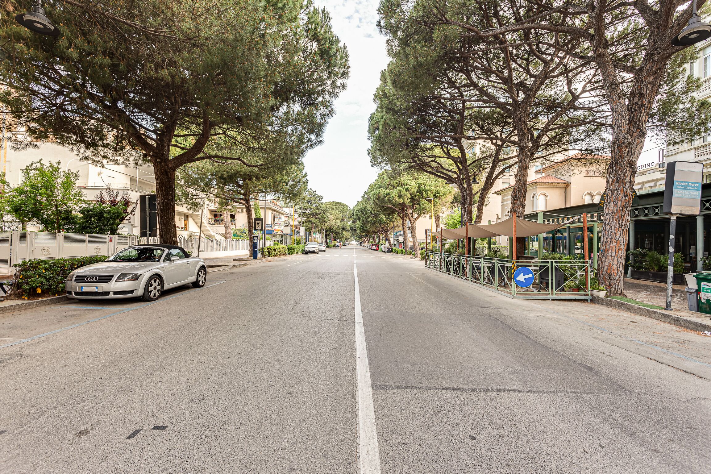 A tree-lined street with a parked car and a building with a sign that reads "Ristorante".