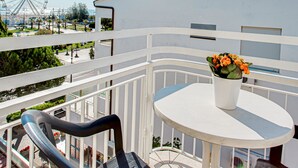 Un balcón con una mesa y sillas blancas, un jarrón de flores y vistas a una noria y un edificio alto.