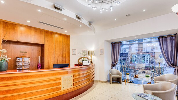 A hotel reception area with a wooden reception desk, a computer, and a view of the city through large windows. - Hotel Villa Maria (Cesenatico)