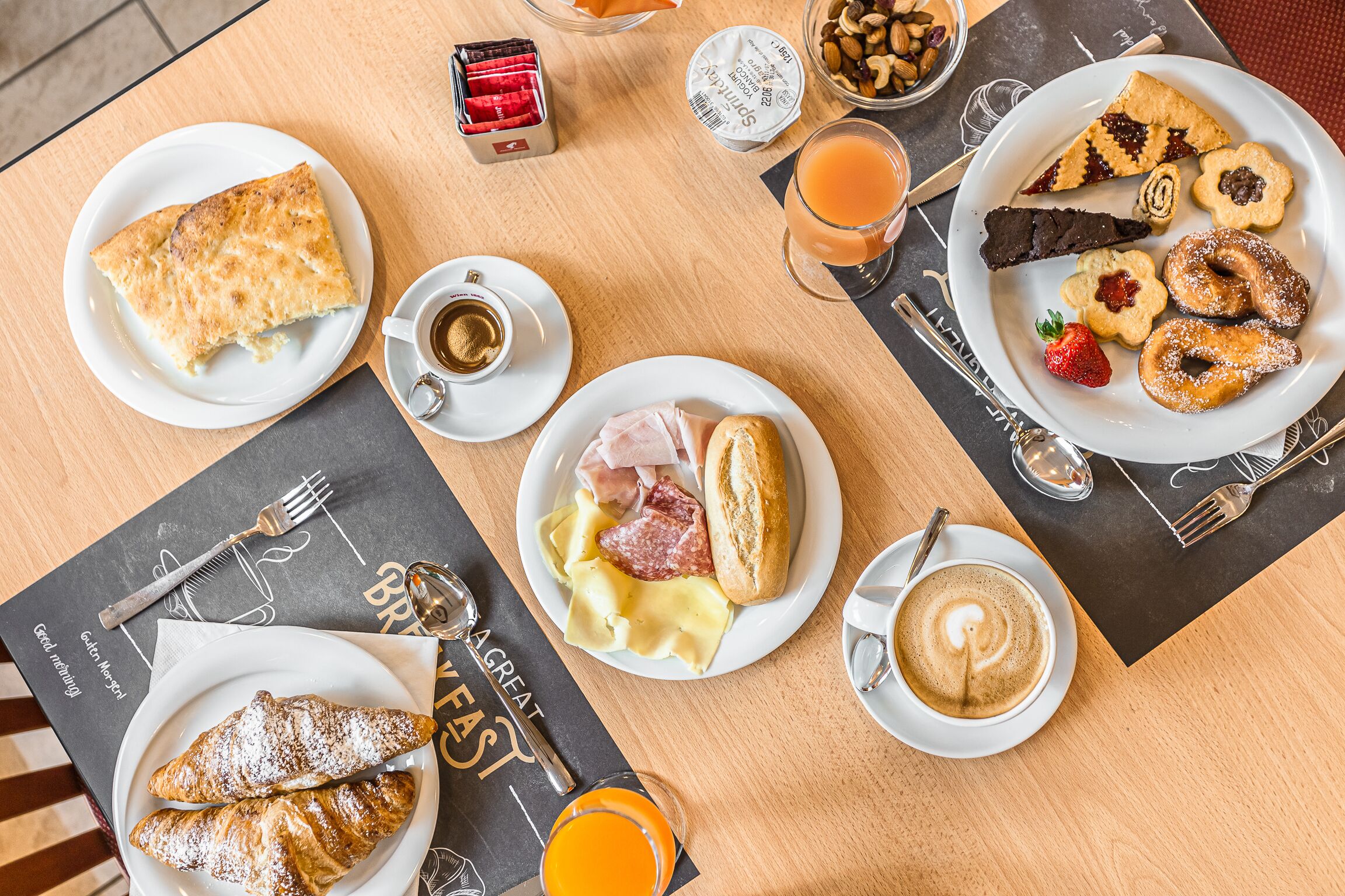 A breakfast setting with various pastries, sandwiches, and beverages on a wooden table.