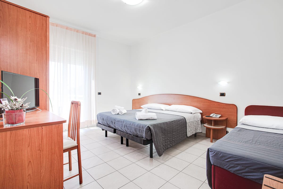 Ein Hotelzimmer mit Bett, Nachttisch, Stuhl, Schreibtisch, Fernseher und einer kleinen Pflanze.