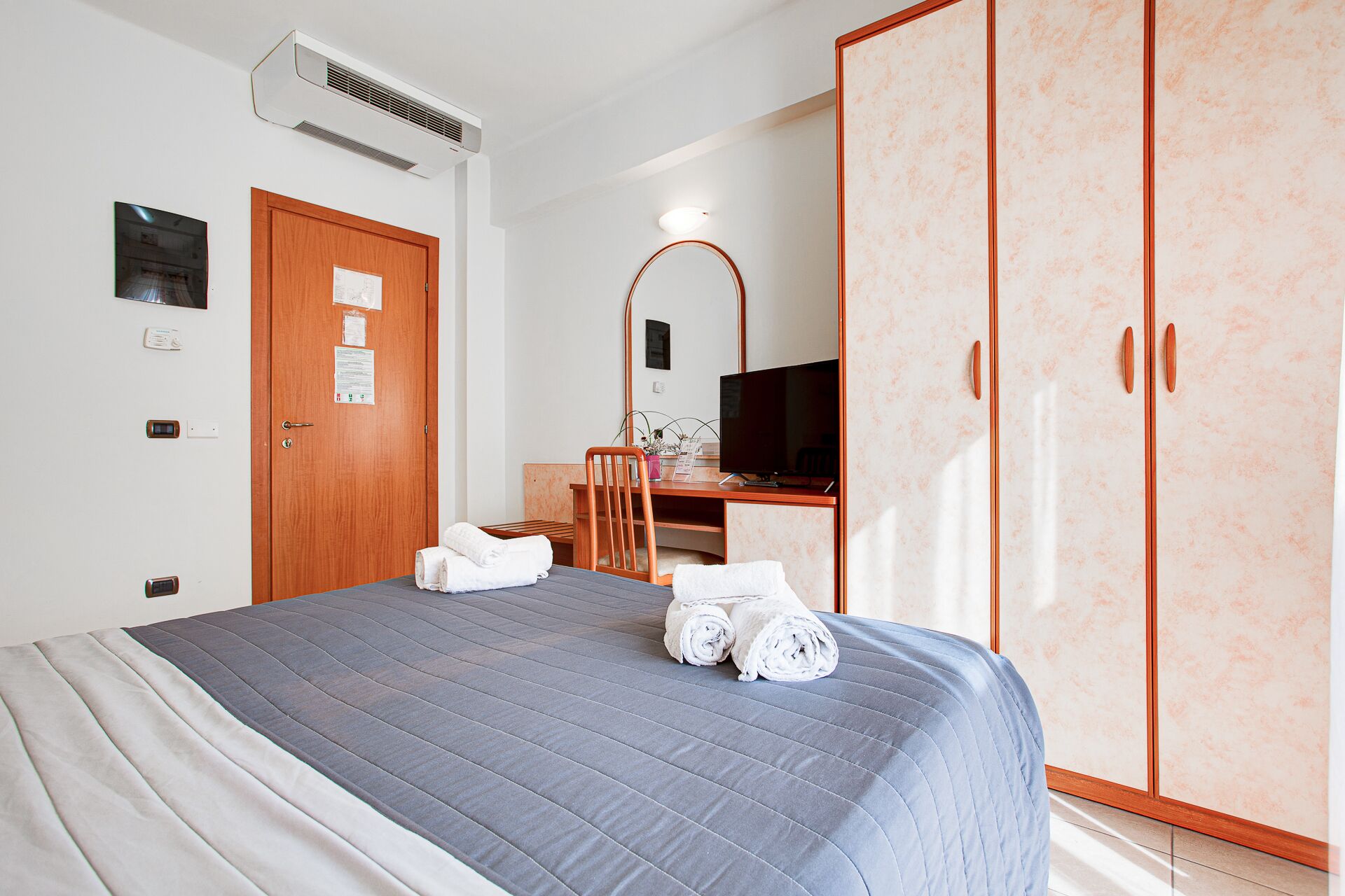 Une chambre d’hôtel comprenant un lit, un bureau avec une chaise, une armoire et un téléviseur.