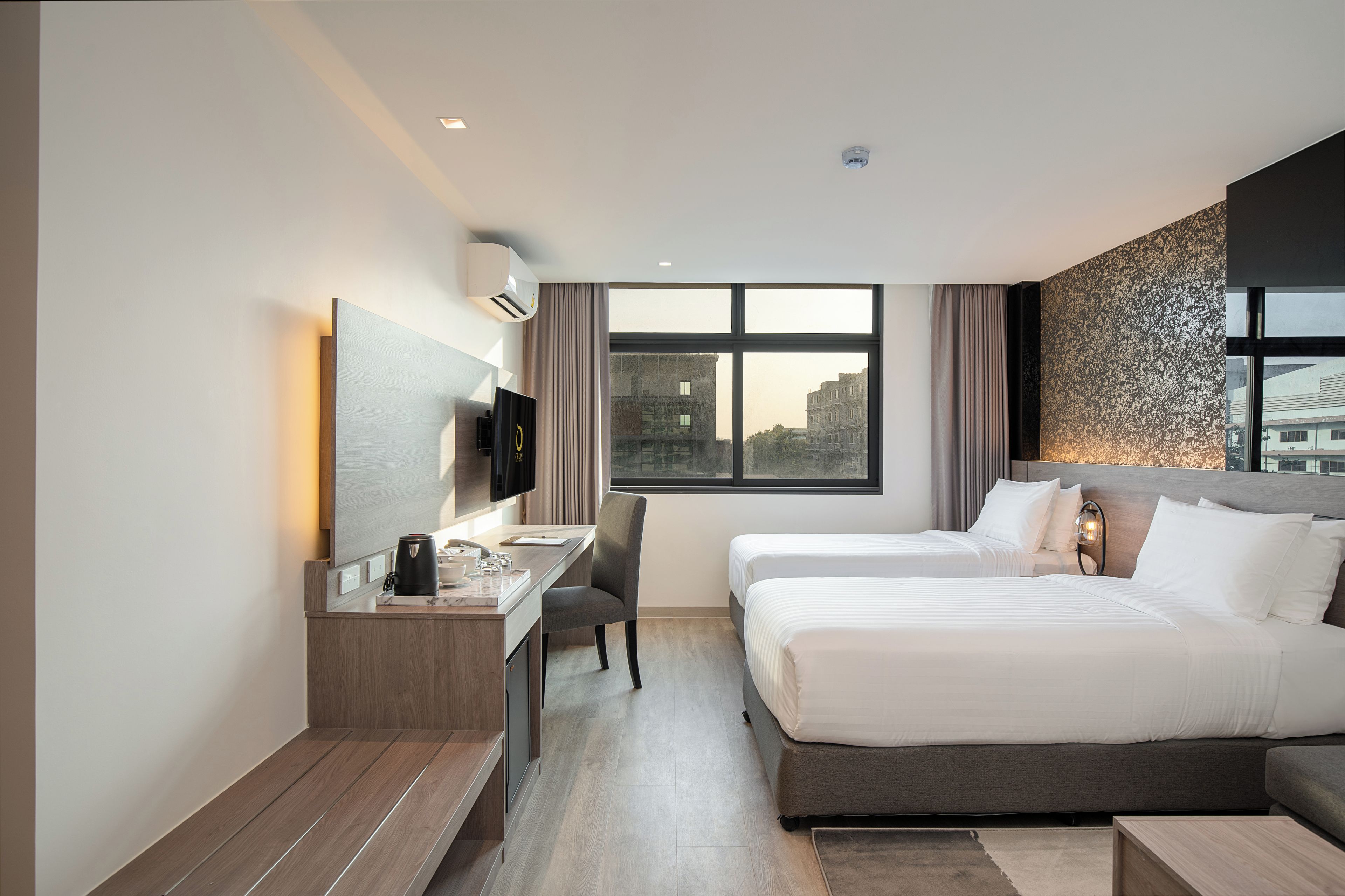 A hotel room with a desk, two beds, a TV, and a large window.