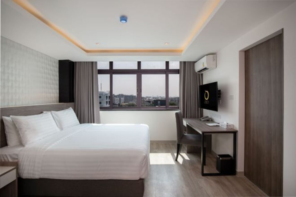 Quarto de hotel moderno com uma cama grande, uma escrivaninha, uma cadeira e uma televisão.