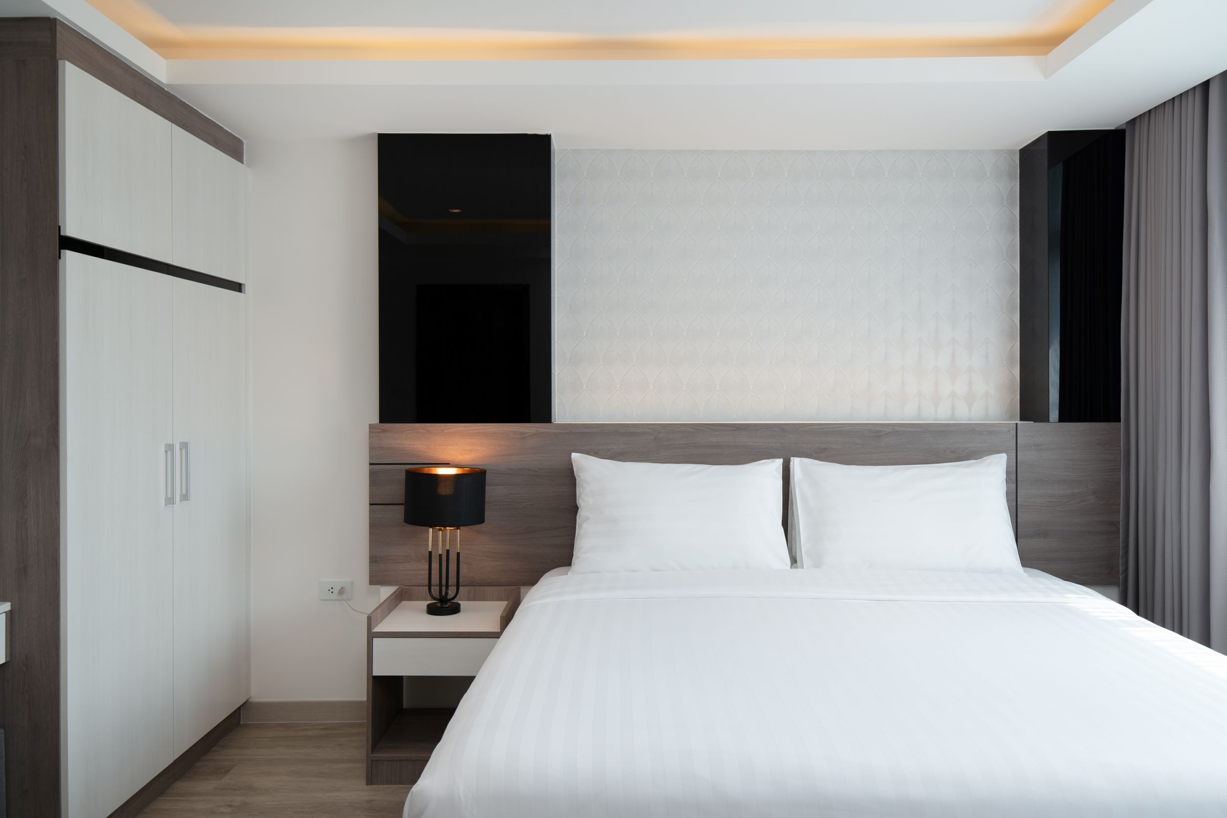 Una habitación de hotel moderna con una cama grande, una mesita de noche con lámpara y un armario.