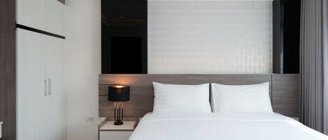 Una habitación de hotel moderna con una cama grande, una mesita de noche con lámpara y un armario.