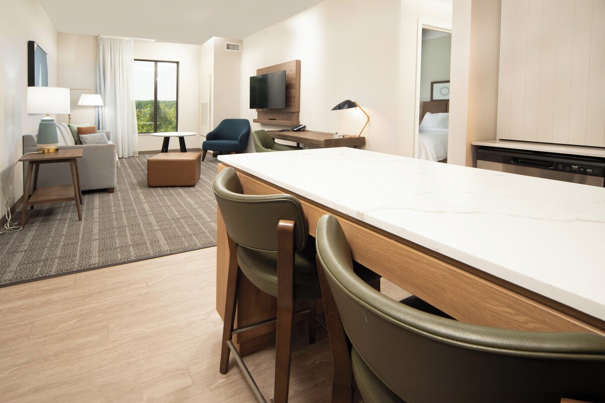 Una habitación de hotel moderna con zona de comedor, sofá, televisión y kitchenette.