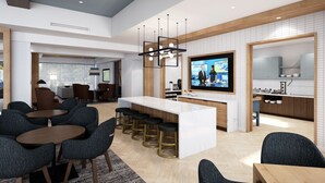 Un hall d’hôtel moderne doté d’un bar central, de différents espaces aménagés pour s’asseoir et d’un écran de télévision.