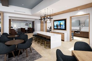 Un moderno vestíbulo de hotel con una zona de bar central, espacios de asiento y una pantalla de televisión.