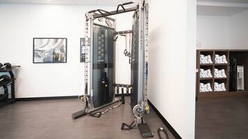 A gym with a weight machine, exercise mats, and towels on shelves.