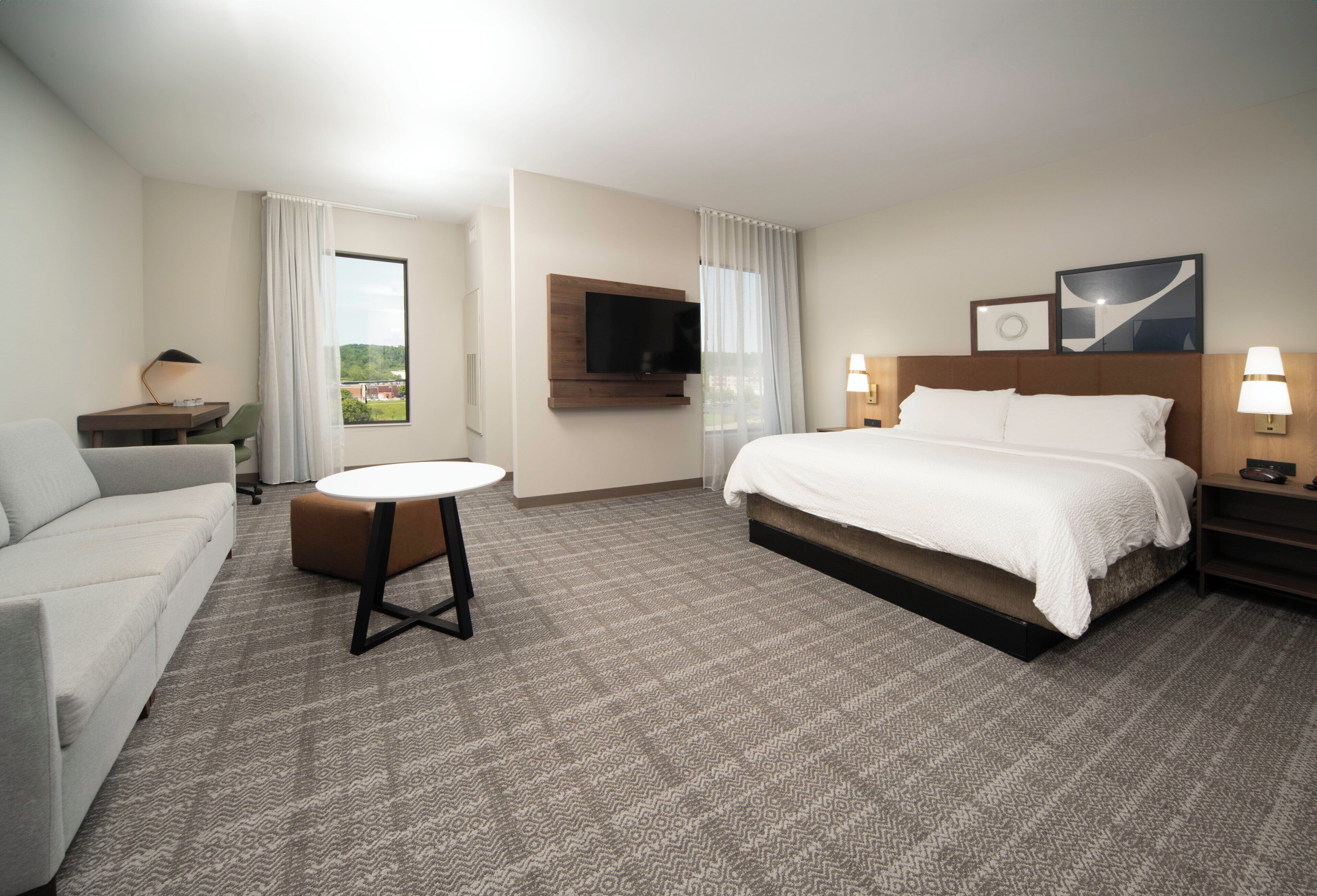 Habitación de hotel con cama, escritorio, silla, televisor y ventana con cortinas.