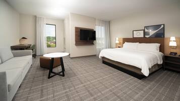 Habitación de hotel con cama, escritorio, silla, televisor y ventana con cortinas.
