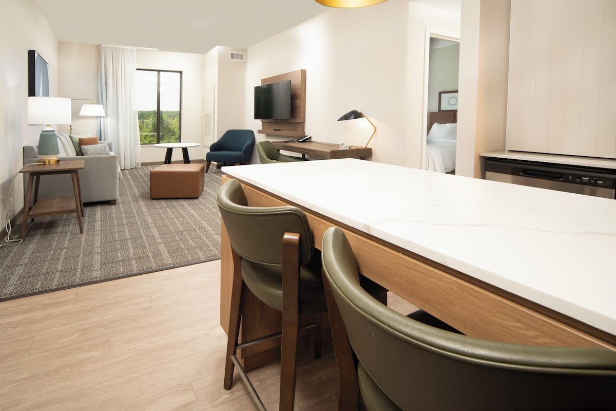 Una habitación de hotel moderna con zona de comedor, sofá, televisión y kitchenette.