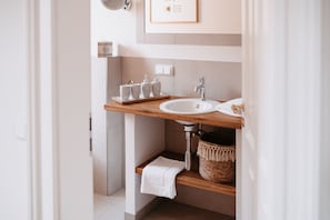 A modern bathroom with a wooden vanity, a sink, and a small shelf with toiletries. - Das Betthupferl - Ihr Aparthotel (Goldbach)