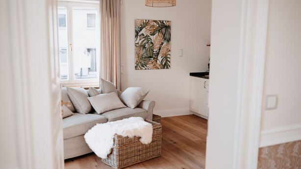 A living room with a sofa, a wicker basket, and a tropical leaf artwork on the wall.