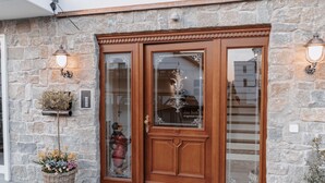 A stone facade with a wooden double door, two wall-mounted lights, and a welcome mat.